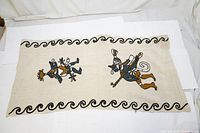 Wide front-facing image showing fully embroidered pillow cover with two traditional Indigenous Southwestern figures and wave patterns on beige fabric.