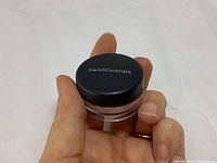 Mini jar of Bare Minerals eyeshadow held in hand showing black top with brand name.
