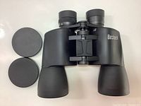 Top view of Bushnell Power View Ultra 10x50 binoculars with lens caps placed beside it on white background