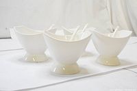 Four white porcelain ice cream bowls each with white ceramic spoon inside. Contemporary design with rounded base and wide top opening shown on a white background.