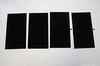 Four black velvet rectangular trays laid out side by side on a white background, two with grooves and two flat with stitched edges.