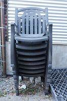 Stack of 8 black high-back plastic chairs leaning against corrugated metal wall outdoors.