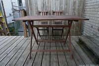 Front view of wooden foldable table and two chairs arranged outdoors on deck.