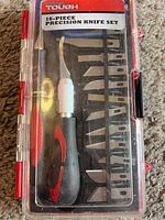 Full view of closed set showing transparent plastic case holding handle and blades, labeled with 'Hyper Tough 16-Piece Precision Knife Set'.