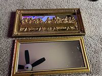 Two rectangular mirrors on carpet, top mirror is plain with gold frame, bottom mirror has Jesus Last Supper 3D relief with matching gold frame.