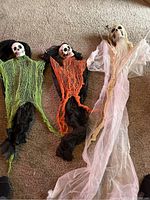 Photo showing all three Halloween decorations together laid on carpet: two small skull demons with colored torn fabric and one large ghost figure in white robe.