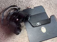 Photo showing black textured binoculars laid out beside an open black case with metal clasp lock.