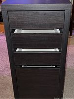 Front view of the black wooden drawer unit with drawers partially open, showing the white interior.