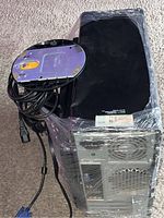 Top and back side view of Dell computer tower showing dent and rear ports, wrapped in plastic with cables on top.
