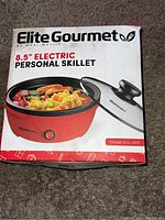 Front view of the original packaging showing the Elite Gourmet 8.5 inch electric personal skillet with glass lid, red exterior, temperature control knob, and label with model EGL-6101.