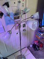 Full view of the floor lamp showing all five arms and shades, plugged in and standing against a white door.