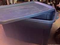 Photo showing the large blue storage tote with lid partially open on carpeted floor.