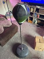 The punching bag standing on its black water-filled base, positioned indoors next to a brown couch and TV.