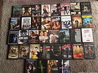 Top-down view of 38 DVDs in cases arranged in rows on carpeted floor showing front covers.