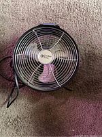 Front view of the black all-metal Comfort Zone fan showing the protective grille, fan blades, and power cord.