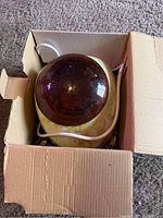 Top view of GiGi wax warmer in its box showing the brown lid and cream body with cord.