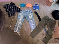 Overview of women's clothing including striped T-shirt, distressed jeans, green pants, multiple beanies, and some scarves laid on carpet.