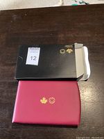 Closed red protective case with gold embossed Royal Canadian Mint logo and original black sleeve opened beside it on wooden surface.