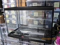 Straight-on front view of one rectangular glass aquarium with black trim containing a heating element and sliding lid. Clear visibility of the tank's interior and structure.