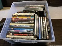Plastic bin containing 31 DVDs arranged vertically showing edges and tops of DVD cases.