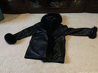 Black leather coat laid flat on floor showing fur collar and cuffs