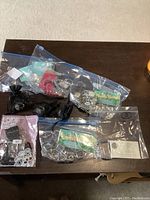 Photo showing several black drawstring pouches containing Arbonne silver rings and assorted packaged items on a dark surface.