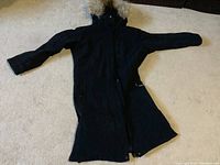 Full view of black Descente coat laid flat showing 3/4 length, long sleeves, and fur-trimmed hood.