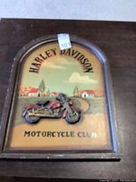 Full view of the Harley Davidson wooden sign showing the 3D motorcycle with painted village background and text.