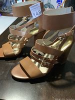 Pair of tan leather high heel sandals with buckle straps and wooden stacked heels.