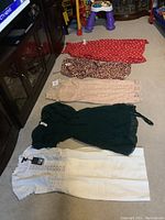 Five women's dresses laid out on floor: red polka dot, leopard print, beige lace, green, and white lace dresses.