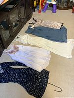 Six women's dresses laid on carpet, new with tags, featuring various colors and styles.