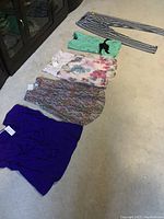 Multiple new women's pants and tops laid on floor, various colors and patterns, new with tags