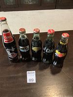 Photo of five full vintage Coca-Cola glass bottles with different sporting and event labels arranged on table