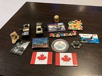 Displaying assorted vintage refrigerator magnets with various motifs including Canadian flags, city images, and souvenirs
