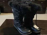 Pair of black SOREL women's winter boots with fur trim on the table, showing side and front details.