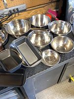 Photo of stainless steel mixing bowls, colander, and baking pans displayed on a metal surface against wood wall background