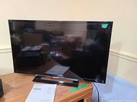 Front view of the 32 inch Sony Bravia TV placed on a wooden surface with remote control and user manual visible in front on the table.