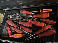 Drawer containing multiple screwdrivers with red, green, and red-yellow handles.