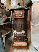 Front view of cylindrical cast iron wood stove showing decorative shield emblem, firebox door and ash pan door.