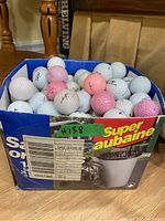Blue cardboard box filled with used golf balls mostly white with some pink ones.