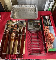 Entire barbecue lot showing cooking pan, utensil set, thermometer packaging, and rotisserie kit box