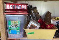 Various bird feeders and large plastic container of bird seed, feeders include plastic hummingbird feeders, metal mesh tube feeders, and wooden birdhouses.