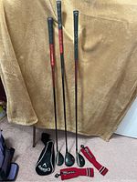 Three Callaway RAZR X HL left-handed golf clubs with visible grips, shafts and heads, laid against brown background with cloth covering.