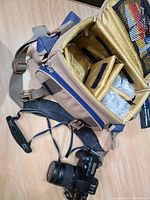 Photo showing tan and blue padded camera bag open with compartments, second lens wrapped inside, and camera body with attached lens outside the bag.