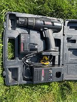 Black cordless drill-driver with battery, battery charger, and power cord inside a molded plastic carrying case with handle.