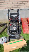 Front view of Craftsman rotary lawn mower with attached collection bag and visible engine and controls next to extra accessories.