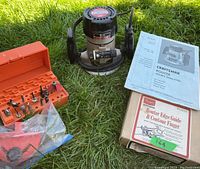 Overview photo showing router, orange case with router bits, owner's manual, and boxed router edge guide and contour finger, all on grass.