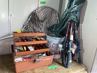Overview photo showing all items together: five fishing rods with reels to the side, metal minnow bucket, fishing net, and open multi-tiered brown tackle box.