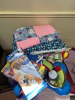 Overall view of pet supplies including blankets, pet toys, blue double feeding dish, and Pedi Paws nail trimmer