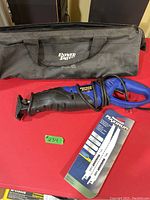 Power Smith reciprocating saw, corded electric with wrapped cord and black Power Smith carrying case on red surface.